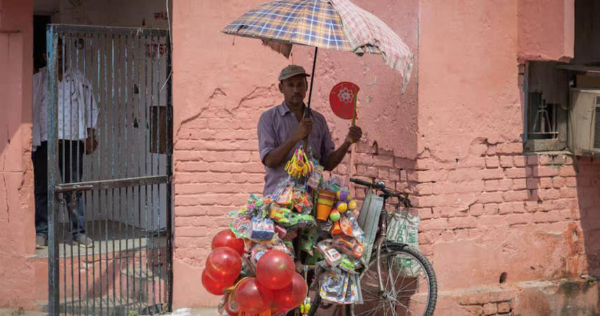在傘下暫時避暑的印度街頭小販。（圖／路透社）
