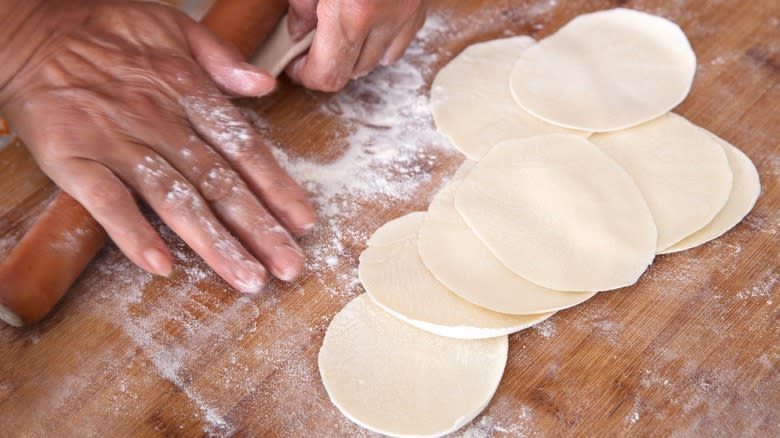hand rolling out dumpling wrappers on a wood cutting board with flour