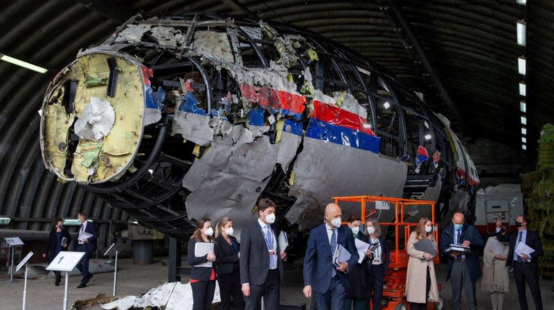 The front of the destroyed plane's fuselage with several people standing in the foreground