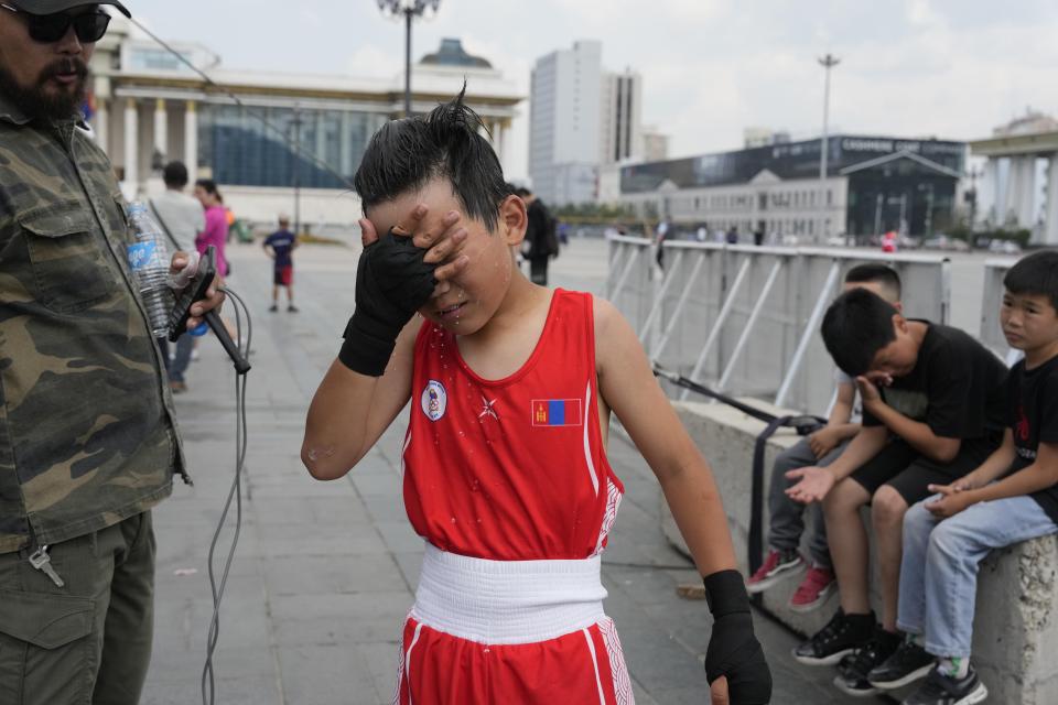 Kherlen Nasantogtokh, left, watches as his twelve-year-old son Gerelt-Od Kherlen wets his face to cool off after winning a bronze medal boxing match on Sukhbaatar Square in Ulaanbaatar, Mongolia, Tuesday, July 2, 2024. Growing up in a Ger district without proper running water, Gerelt-Od fetched water from a nearby kiosk every day for his family. Carrying water and playing ball with his siblings and other children made him strong and resilient. (AP Photo/Ng Han Guan)