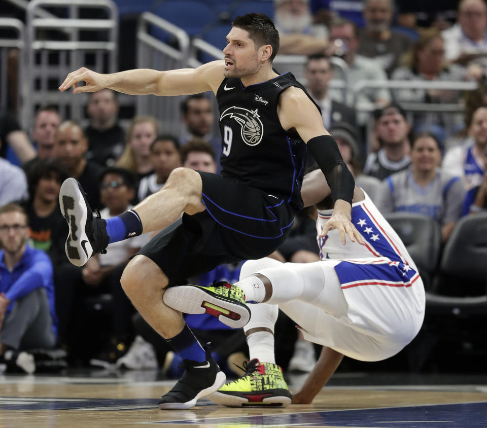 Orlando Magic's Nikola Vucevic (9) falls backward as he trips over Philadelphia 76ers' Joel Embiid during the first half of an NBA basketball game, Monday, March 25, 2019, in Orlando, Fla. (AP Photo/John Raoux)