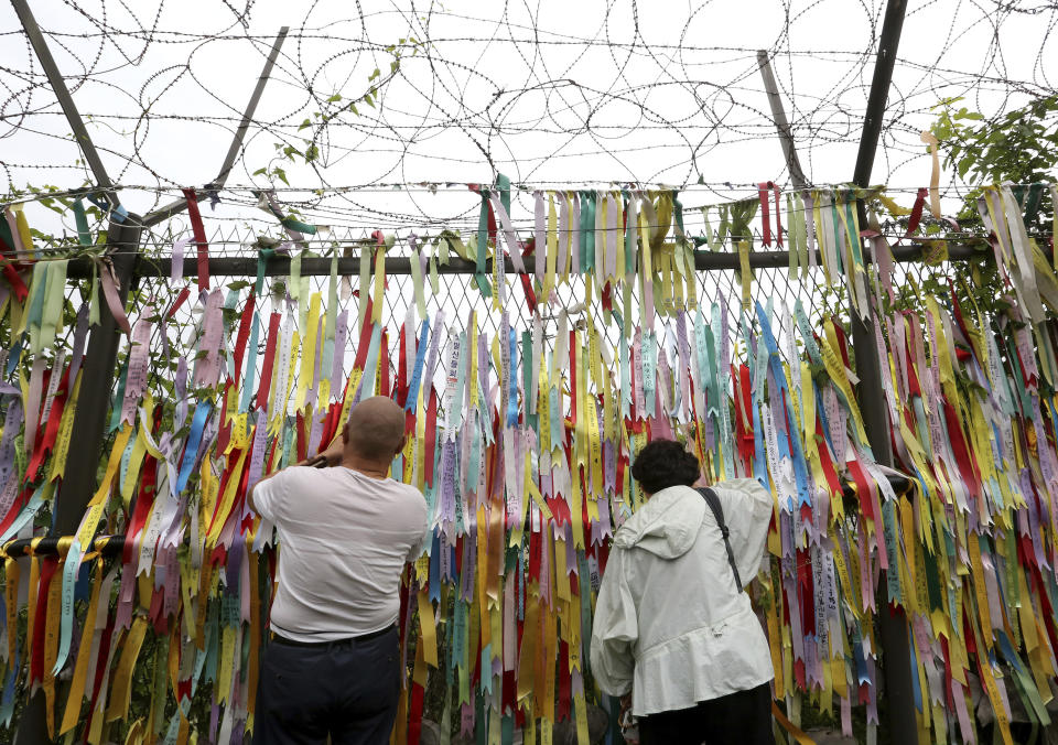 Visitors look through a wire fence decorated with ribbons written with messages wishing for the reunification of the two Koreas at the Imjingak Pavilion, near the demilitarized zone of Panmunjom, in Paju, South Korea, Thursday, June 20, 2019. Chinese President Xi Jinping departed Thursday morning for a state visit to North Korea, where he's expected to talk with leader Kim Jong Un about his nuclear program while negotiations have stalled with Washington. (AP Photo/Ahn Young-joon)