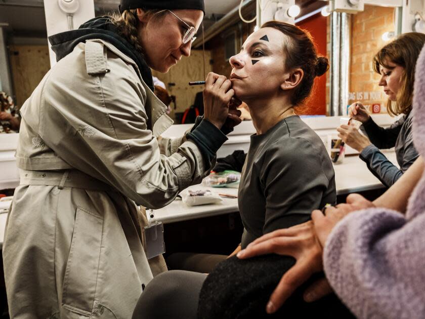 A woman puts makeup on an actor playing the Fool in 