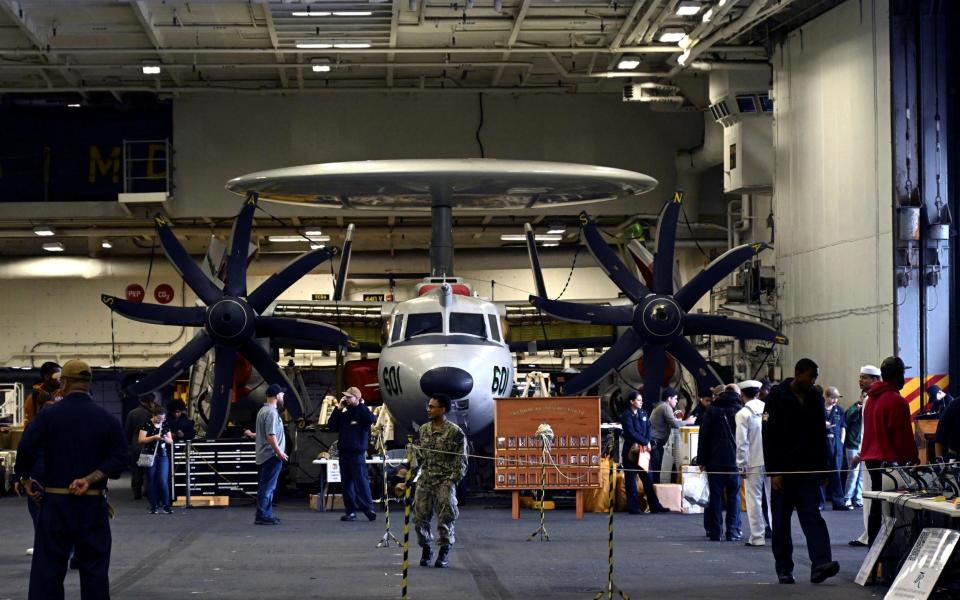 Crew members walk near aircraft in the hangar of the Theodore Roosevelt