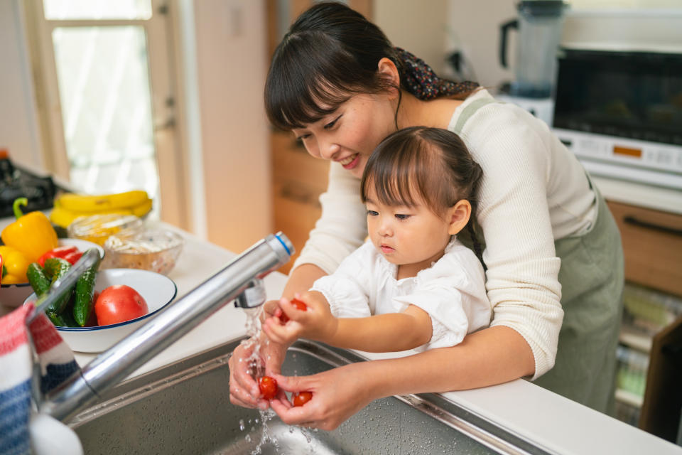 A mother is helping her small daughter washing vegetables and encouraging her for healthy eating.