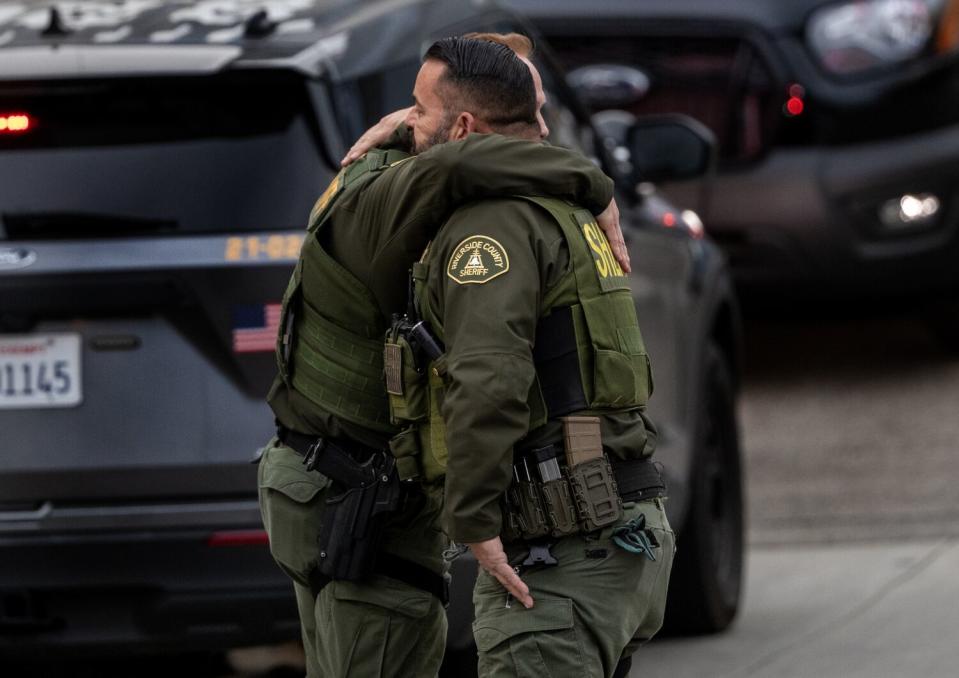 Two sheriff's deputies in uniform embrace in a parking lot.