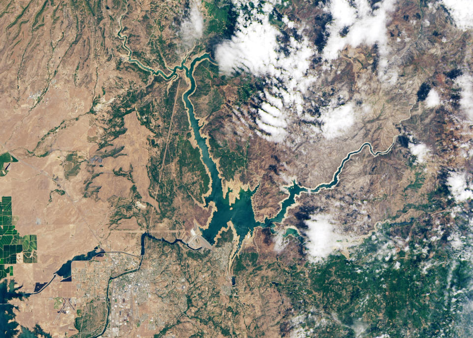 California's Lake Oroville in June 2020. Water flowing from the Sierra Nevada mountains is collected in the dam and then distributed to farms in the Central Valley. Drought has lowered water levels in the reservoir, while wildfires have burned the surrounding forest.  