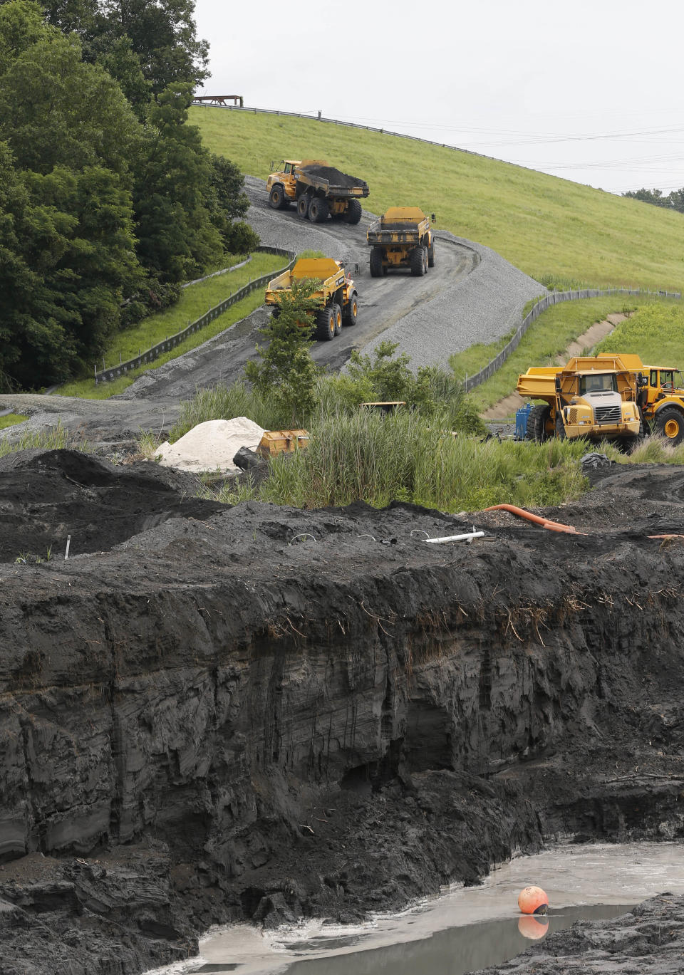 FILE - In this Friday June 26, 2015 file photo, trucks climb a hill as they haul coal ash from one retention pond, foreground, to a permanent pond at the Dominion Power's Possum Point Power Station in Dumfries, Va. As Virginia and its public utilities struggle to cope with the coal ash buried in pits and ponds across the state, tons more of the industrial byproduct is being imported each year. (AP Photo/Steve Helber, File)