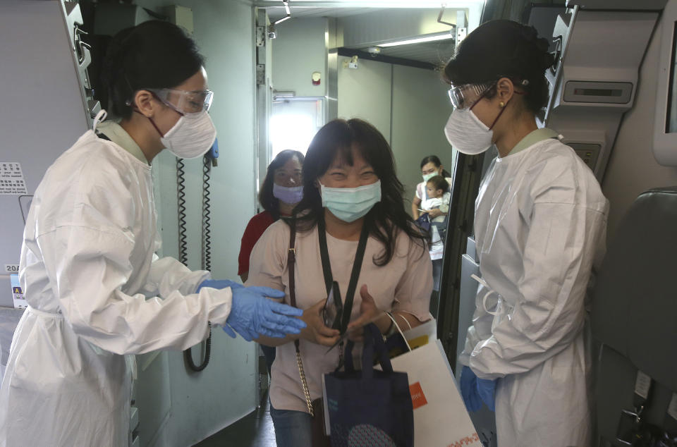 Participants are greeted by flight attendants in protective suits during a mock trip abroad at Taipei Songshan Airport in Taipei, Taiwan, Tuesday, July 7, 2020. Dozens of would-be travelers acted as passengers in an activity organized by Taiwan’s Civil Aviation Administration to raise awareness of procedures to follow when passing through customs and boarding their plane at Taipei International Airport. (AP Photo/Chiang Ying-ying)