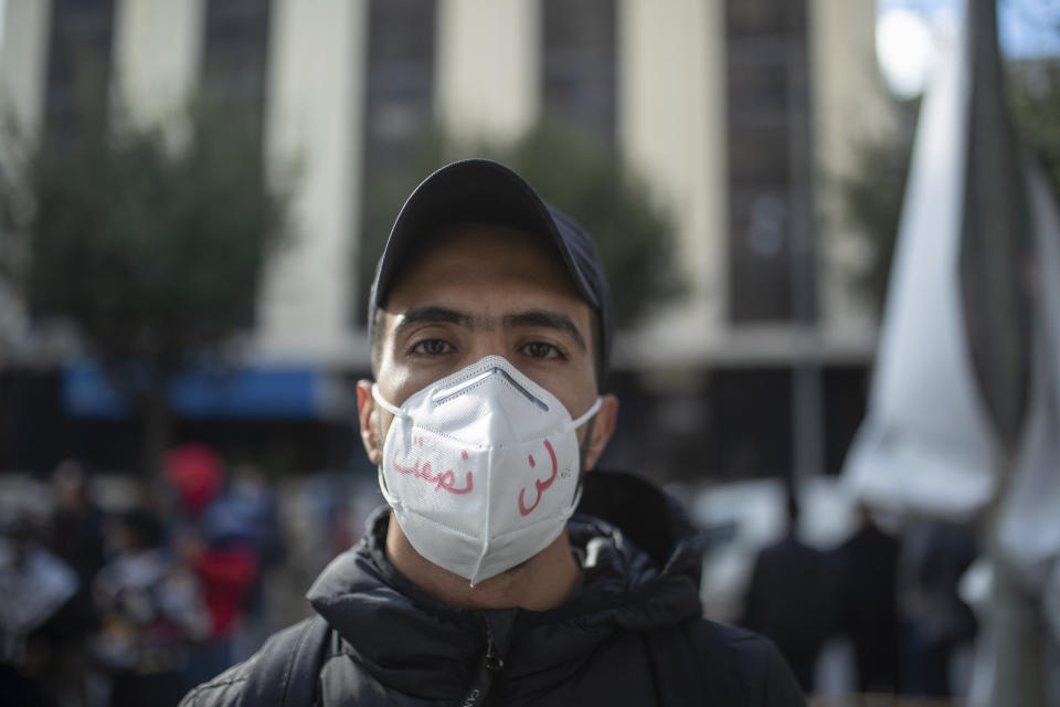 A young man wearing a face mask poses for a portrait during a protest on the tenth anniversary of the uprising that toppled longtime autocrat Ben Ali, during to a national lockdown after a surge in COVID-19 cases, in Tunis, Thursday, Jan. 14, 2021. Writing in Arabic on facemark reads "We will not be silenced." Tunisia is commemorating the 10th anniversary since the flight into exile of its iron-fisted leader, Zine El Abidine Ben Ali, pushed from power in a popular revolt that foreshadowed the so-called Arab Spring. But there will be no festive celebrations Thursday marking the revolution in this North African nation, ordered into lockdown to contain the coronavirus. (AP Photo/Mosa'ab Elshamy)