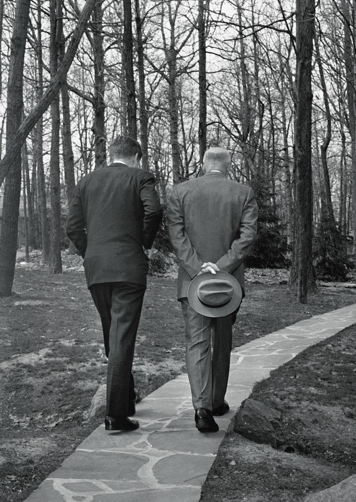 FILE - In this April 22, 1961, file photo, President John F. Kennedy, left, walks along a path at Camp David near Thurmont, Md., with former President Dwight D. Eisenhower as the two met to discuss the Bay of Pigs invasion. For U.S. presidents, Camp David offers a respite from Washington where they can shed their ties and relax with family. The compound in the Maryland mountains just 60 miles from the capital features everything from a bowling alley to an archery range. It’s been used by every president since Franklin Delano Roosevelt first went there in 1943 as a personal hideaway, and has been the site of major diplomatic negotiations and policy discussions. (AP Photo/Paul Vathis, File)
