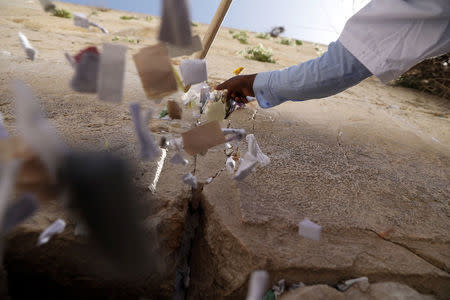 A man uses a stick to clear notes placed in the cracks of the Western Wall, Judaism's holiest prayer site, to create space for new notes ahead of the Jewish holiday of Passover, in Jerusalem's Old City, March 20, 2018. REUTERS/Ammar Awad