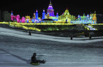 A visitor sleighs down a snow slope near ice sculptures during the lights testing period of the 13th Harbin Ice and Snow World in Harbin, Heilongjiang province December 25, 2011. The Harbin International Ice and Snow Festival will be officially launched on January 5, 2012. Picture taken December 25, 2011. REUTERS/Sheng Li (CHINA - Tags: ENVIRONMENT SOCIETY TRAVEL)