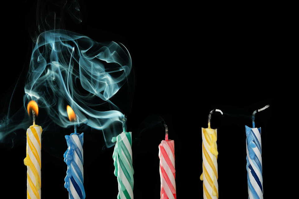 Five blown-out birthday candles still emitting smoke, with only two candles remaining lit