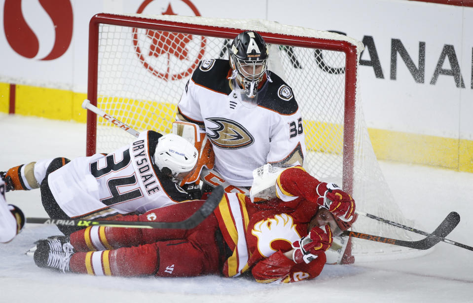 Anaheim Ducks' Jamie Drysdale, left, checks Calgary Flames' Blake Coleman, right, into goalie John Gibson during overtime of an NHL hockey game in Calgary, Alberta, Monday, Oct. 18, 2021. (Jeff McIntosh