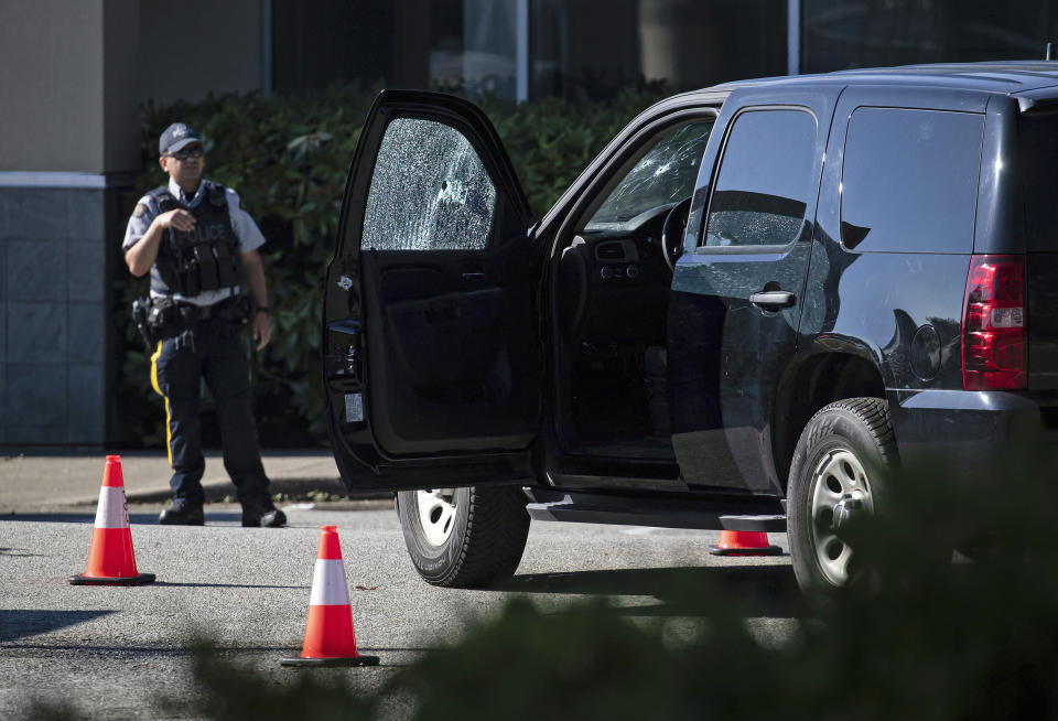 A police officer stands near a RCMP vehicle with bullet holes in the windshield and driver's side window at the scene of a shooting in Langley, British Columbia, Monday, July 25, 2022. (Darryl Dyck/The Canadian Press via AP)