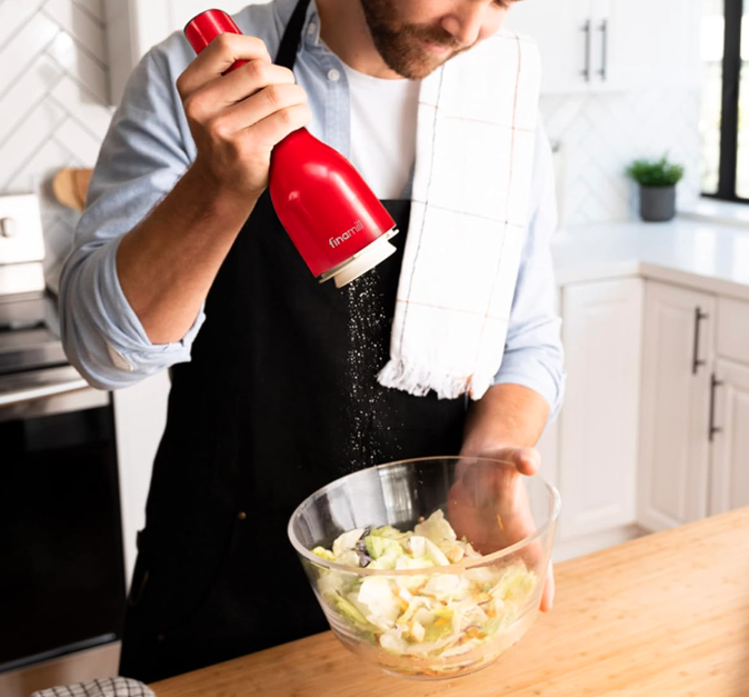 man using spice grinder over a salad.