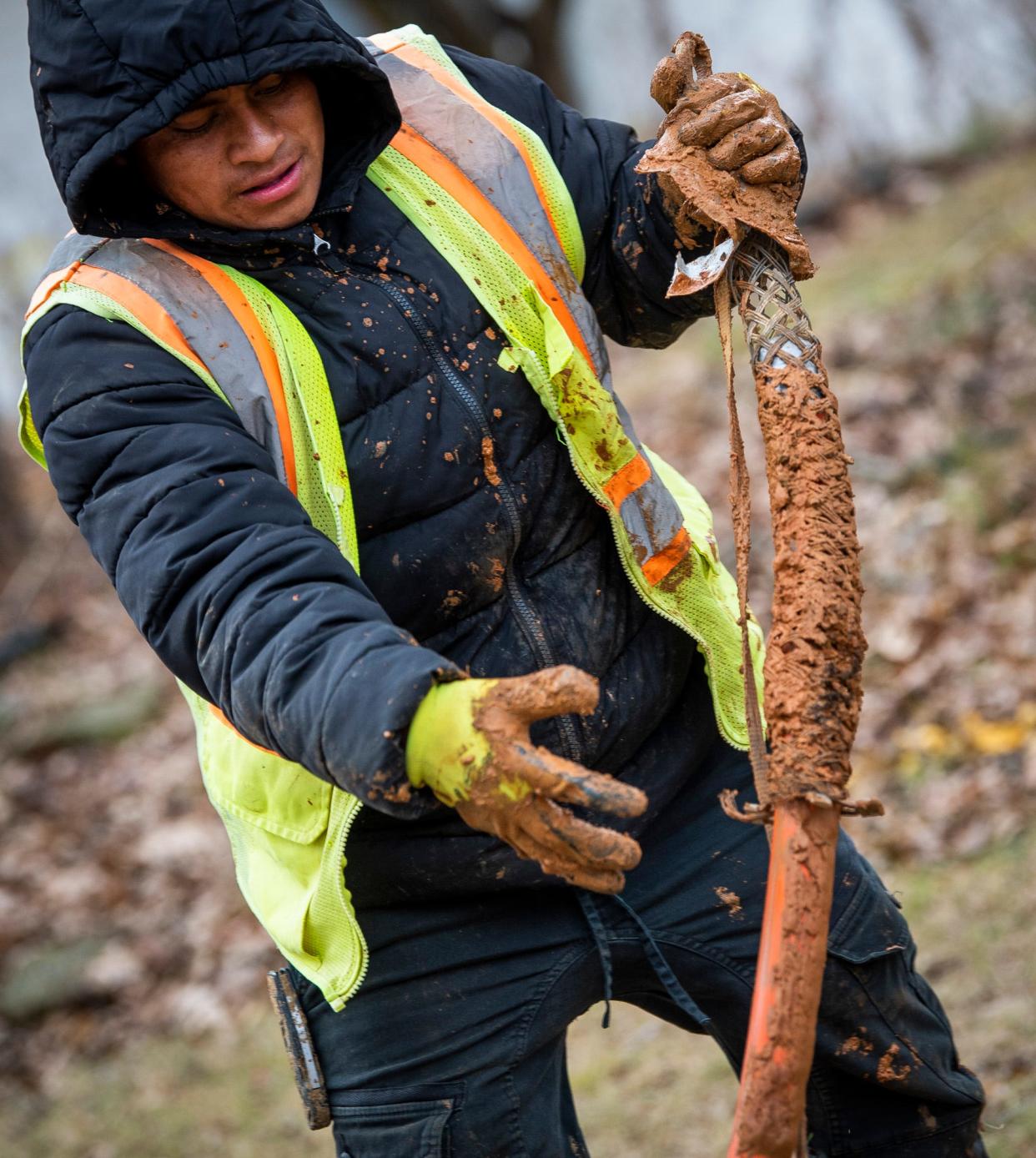 A mud-splattered Jose Dionicio pulls a fiber cable through a hole along Glenwood Avenue on Monday, Dec. 5, 2022.