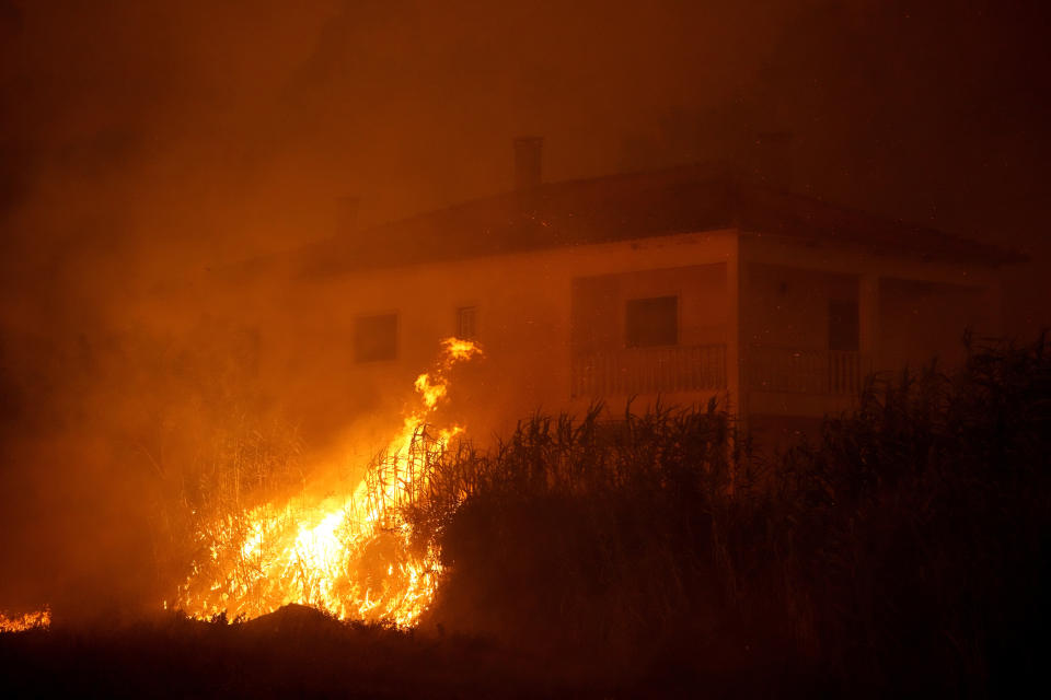 A forest fire reaches an empty house as smoke darkens the sky in the village of Bemposta, near Ansiao, central Portugal, Wednesday, July 13, 2022. Thousands of firefighters in Portugal continue to battle fires all over the country that forced the evacuation of dozens of people from their homes. (AP Photo/Armando Franca)