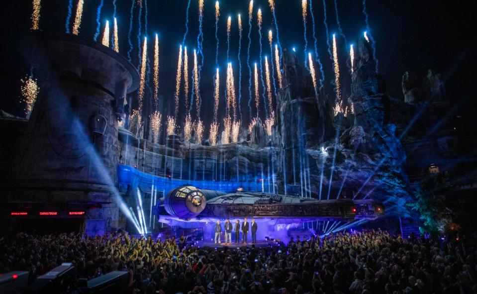 Blue and white fireworks shoot into the night air above a Millennium Falcon.