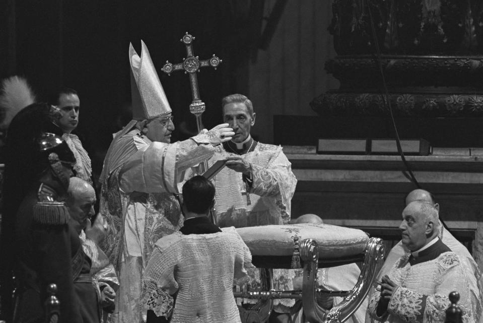 FILE - Pope John XXIII waves a hand in blessing at Roman Catholic Ecumenical Council at St. Peter's Basilica in Vatican City, Oct. 11, 1962. The Council opened earlier in the day. In the background is Monsignor Enrico Dante, prefect of the Vatican ceremonial office. (AP Photo/Raoul Fornezza, File)