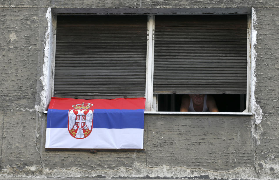 A man peers through window decorated with a Serbian flag during a 60-hour curfew in Belgrade, Serbia, Friday, April 10, 2020. Serbia has introduced some of the harshest measures in Europe as part of efforts to curb the spread of the new coronavirus. The rules include a ban for all citizens over 65 years old from leaving their homes and daily and weekend curfews. The new coronavirus causes mild or moderate symptoms for most people, but for some, especially older adults and people with existing health problems, it can cause more severe illness or death. (AP Photo/Darko Vojinovic)