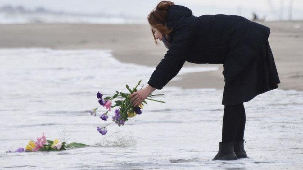 Una mujer pone flores en la orilla del mar para orar por las víctimas del terremoto y tsunami de 2011 en Sendai, norte de Japón, el 11 de marzo de 2016.