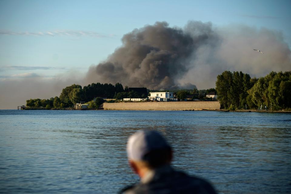 A fisherman watches smoke rise after Russian forces launched a missile attack on a military unit in the Vyshhorod district on the outskirts of Kyiv, Ukraine, Thursday, July 28, 2022. (AP Photo/David Goldman)