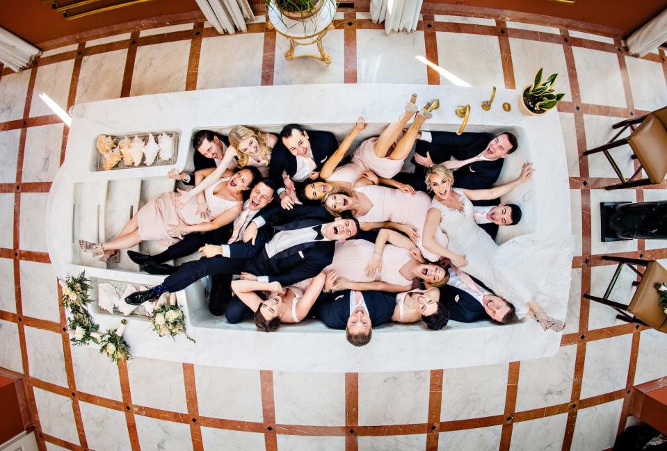 A bridal party lays in a massive bathtub together.
