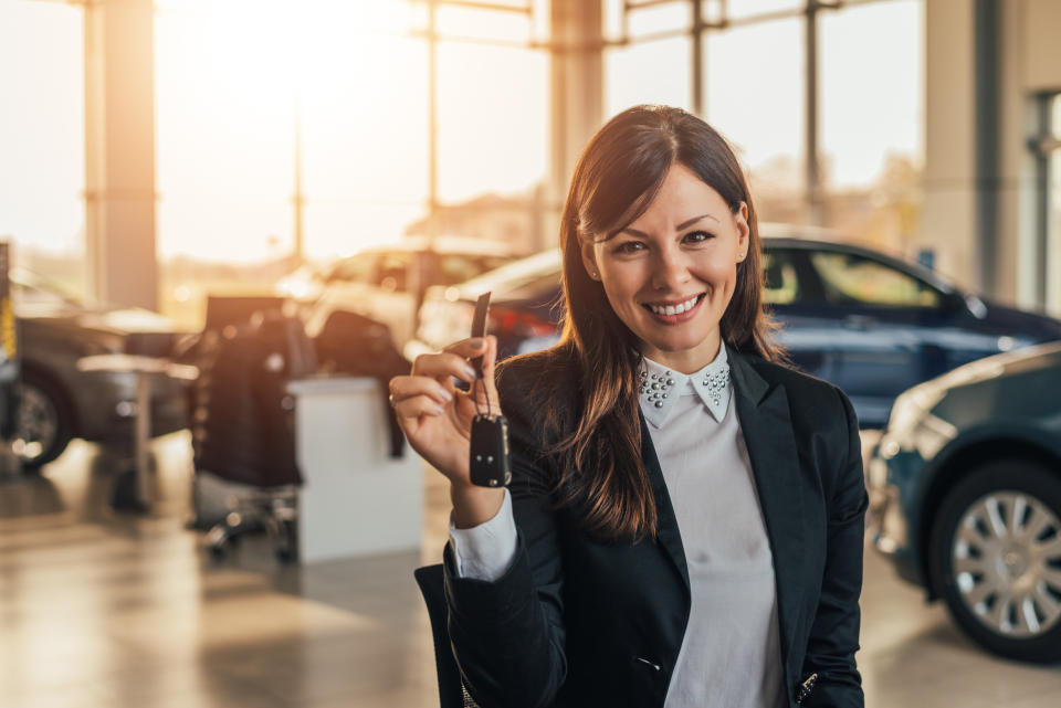 A woman holds up the keys to a new car at a dealership.