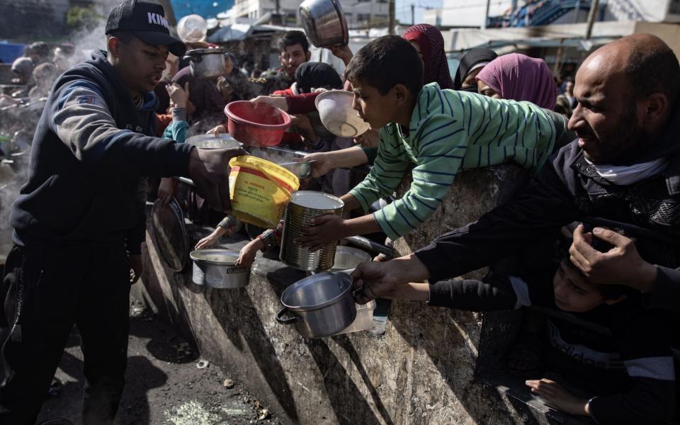 Displaced Palestinians hold empty pots and buckets as they wait to receive food in Southern Gaza's Rafah refugee camp