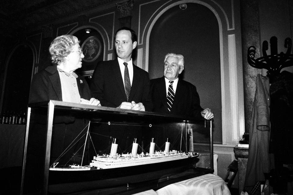 a black and white photo of three people speaking while standing behind a model of the titanic