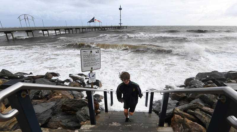 A young boy runs up steps to avoid a wave as high tide and a storm surge at Brighton Jetty as a storm front starts to hit Adelaide's coast line.