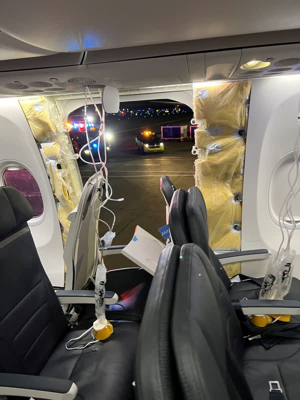 FILE PHOTO: Passenger oxygen masks hang from the roof next to a missing window and a portion of a side wall of an Alaska Airlines Flight 1282, in Portland, Oregon