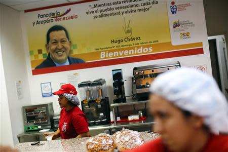 Women work at a bakery as a banner of the late Venezuelan President Hugo Chavez is seen in Ciudad Caribia outside Caracas September 26, 2013. REUTERS/Jorge Silva