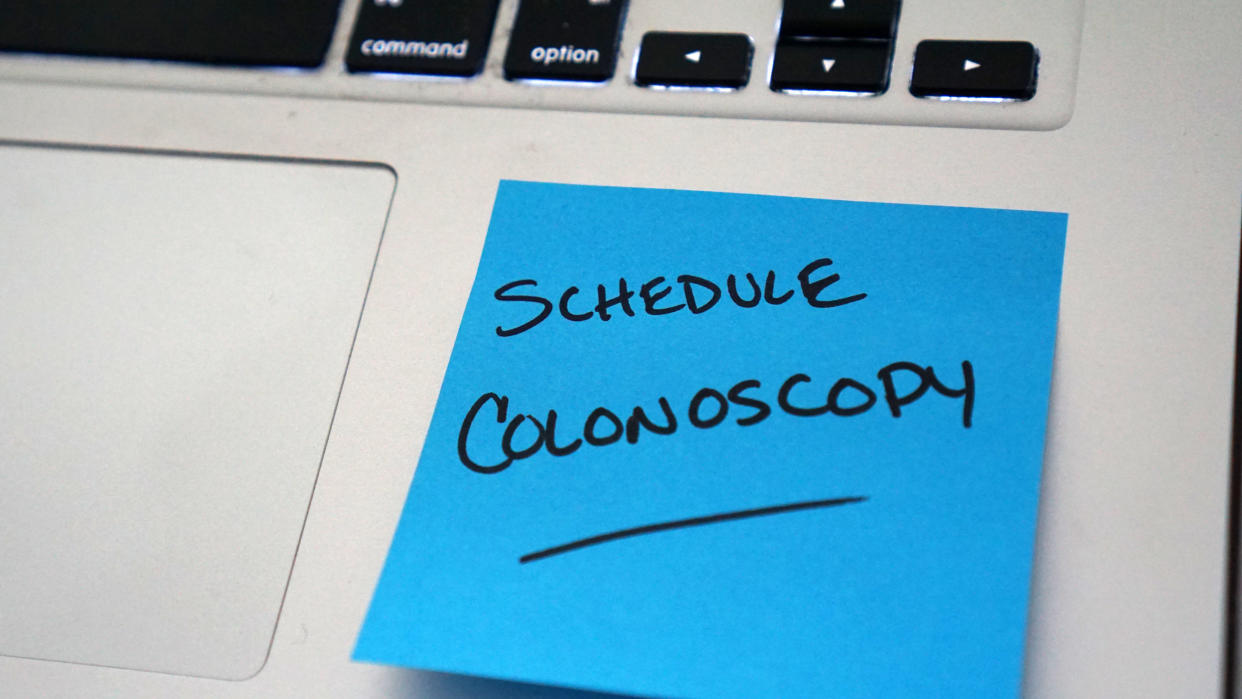 A sticky note attached to a laptop computer reads: Schedule colonoscopy.