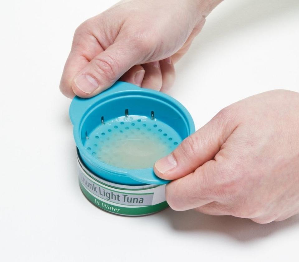 Person's hands using a can strainer on a tuna can