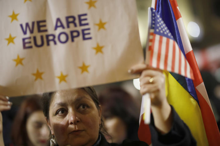 A woman holding flags, including that of the U.S., and a &#x00201c;We are Europe&#x00201d; sign participates in a protest.