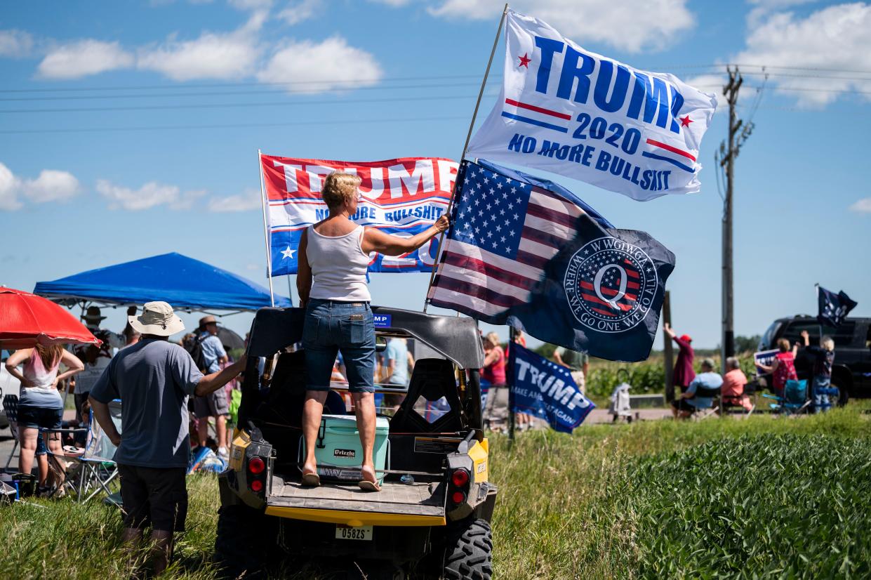 A woman holds a Trump 2020 flag and a QAnon flag outside of Mankato Regional Airport in Minnesota as President Donald Trump makes a campaign stop on Aug. 17, 2020.