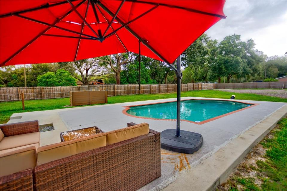 The pool and a red umbrella over outdoor couches at a house in florida