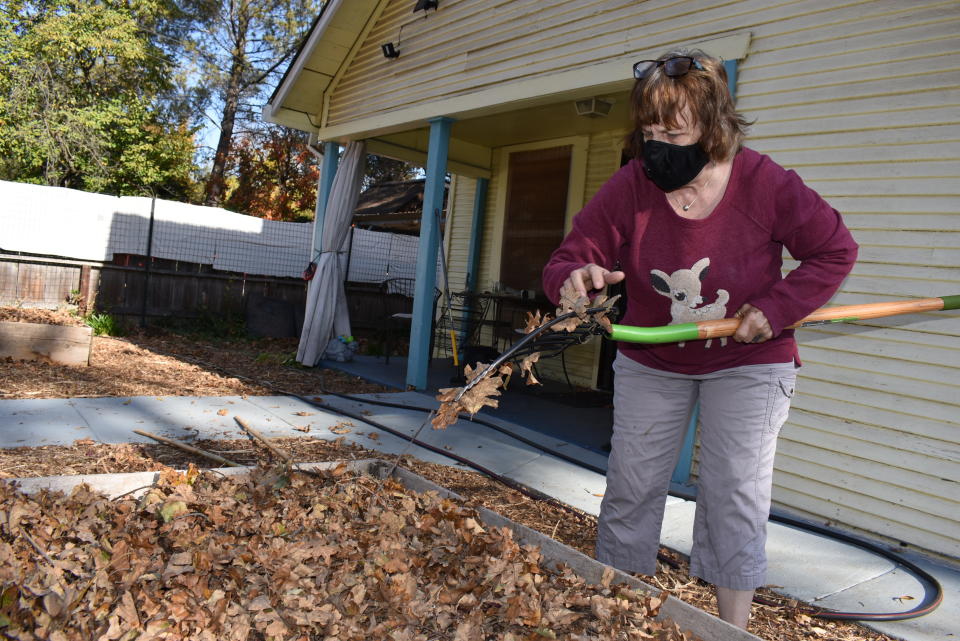 In this Friday, Nov. 22, 2019, photo, Elizabeth Watling spreads leaves over her garden to prepare it for winter while wearing a mask to protect against dust in Chico, Calif. Watling says her throat has been easily irritated since she was exposed to the huge smoke plume from a wildfire that destroyed the nearby town of Paradise the year before, killing 85 people and destroying more than 14,000 homes. (AP Photo/Matthew Brown)