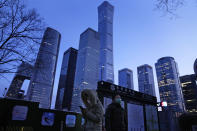 A resident looks at her phone near skyscrapers at the central business district in Beijing, China, Wednesday, Jan. 26, 2022. Richer, more heavily armed and openly confrontational, China has undergone history-making change since the last time it was an Olympic host in 2008. (AP Photo/Ng Han Guan)