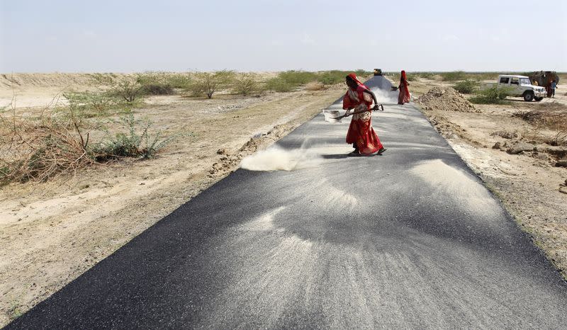 Women labourers throw dust on a road tarmac under construction at Bharadva village in Gujarat