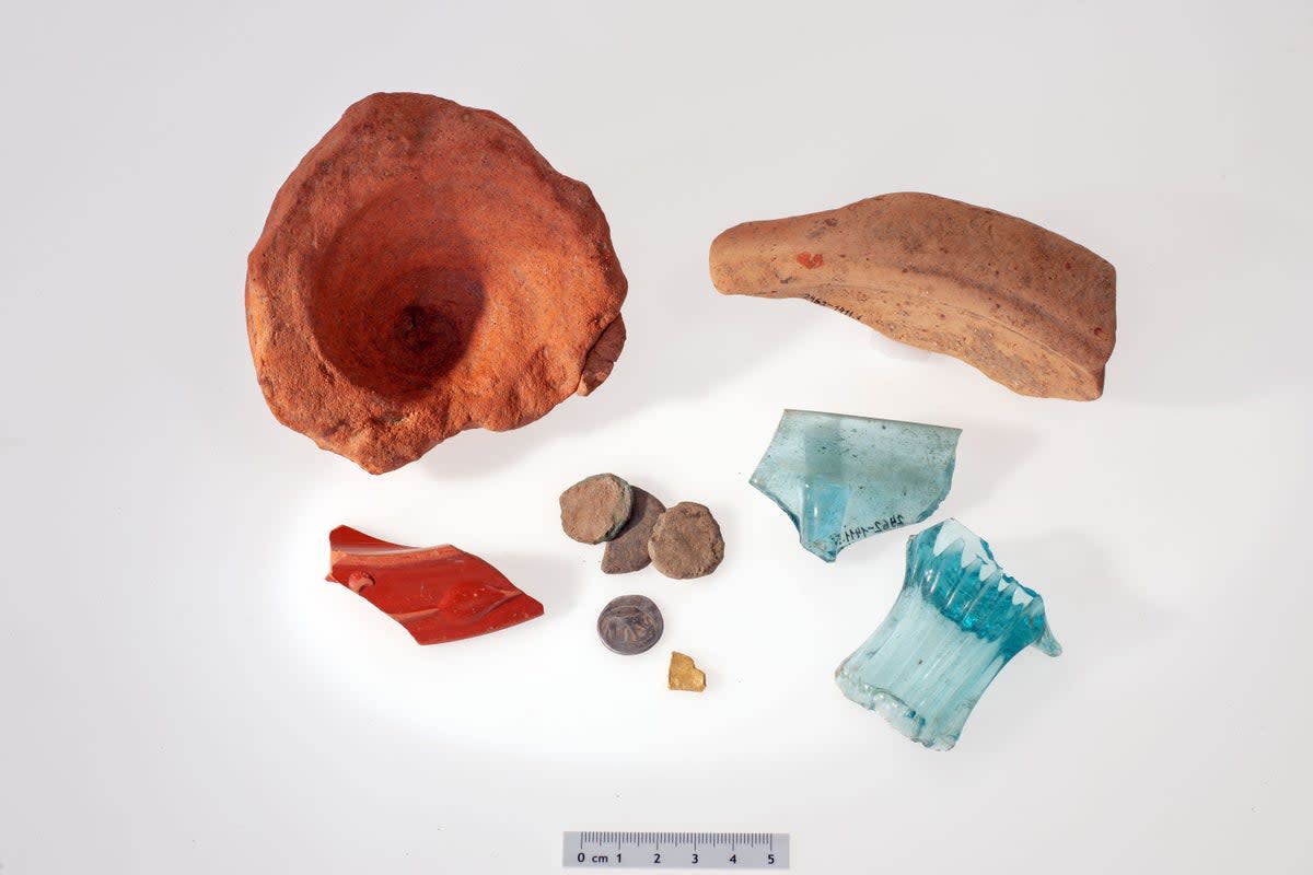 Small selection of Roman finds (from top left to bottom right): An amphora base, the shard of a rubbing bowl, the edge piece of a small bowl of Roman tableware with red coating (Terra Sigillata), four coins in found state, one of them made of silver by Julius Caesar, fragment of a gold object, pieces of a square bottle and a rib bowl made of blue glass (ADA Zug, Res Eichenberger)