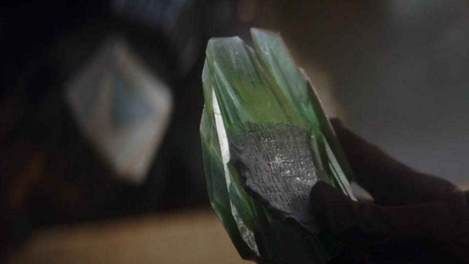 the Armorer holds a Mandalore relic with writing encased in green glass on The Mandalorian
