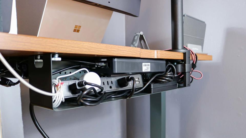 The Branch Duo Standing Desk's cable management tray filled with a surge protector and various cables