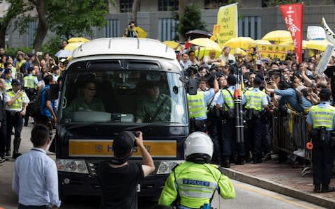 Four of the activists are driven away from court on Wednesday as supporters rally outside carrying yellow umbrellas, a symbol of the pro-democracy movement in Hong Kong - Credit: &nbsp;JEROME FAVRE/EPA-EFE/REX