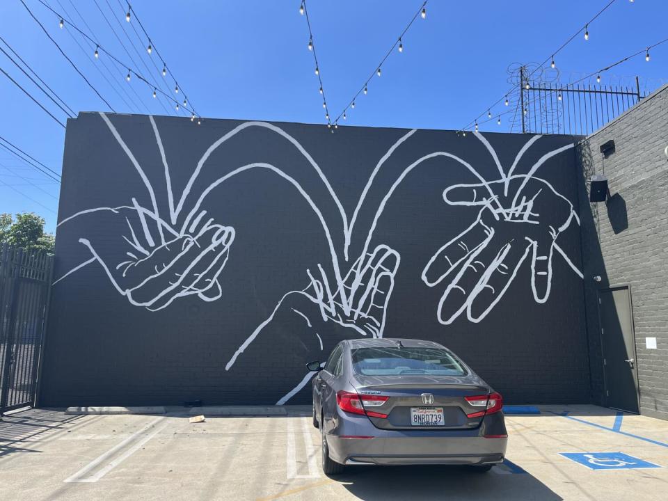 A black and white mural on a building facade shows lines bouncing between three extended hands