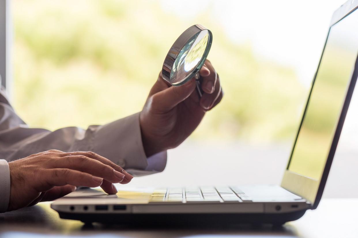 man holding magnifying glass over laptop