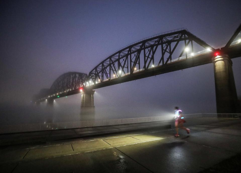 A runner jogs along sidewalk at Waterfront Park as fog rolls into metro Louisville on January 25, 2024